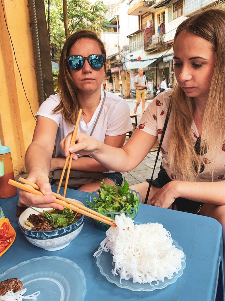 Ja a Miška sa obe cez seba naťahujeme za iným jedlom pri malom plastovom modrom stole s čínskymi paličkami v rukách