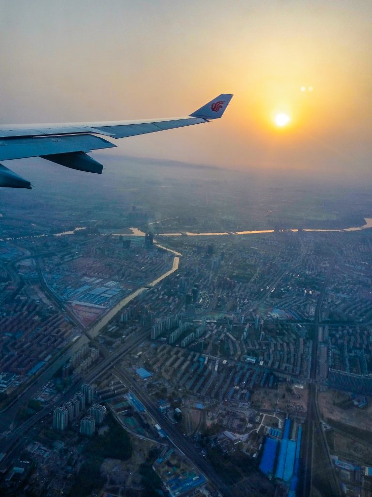 Krídlo lietadla značky Air China pri západe slnka fotené nad mestom Peking