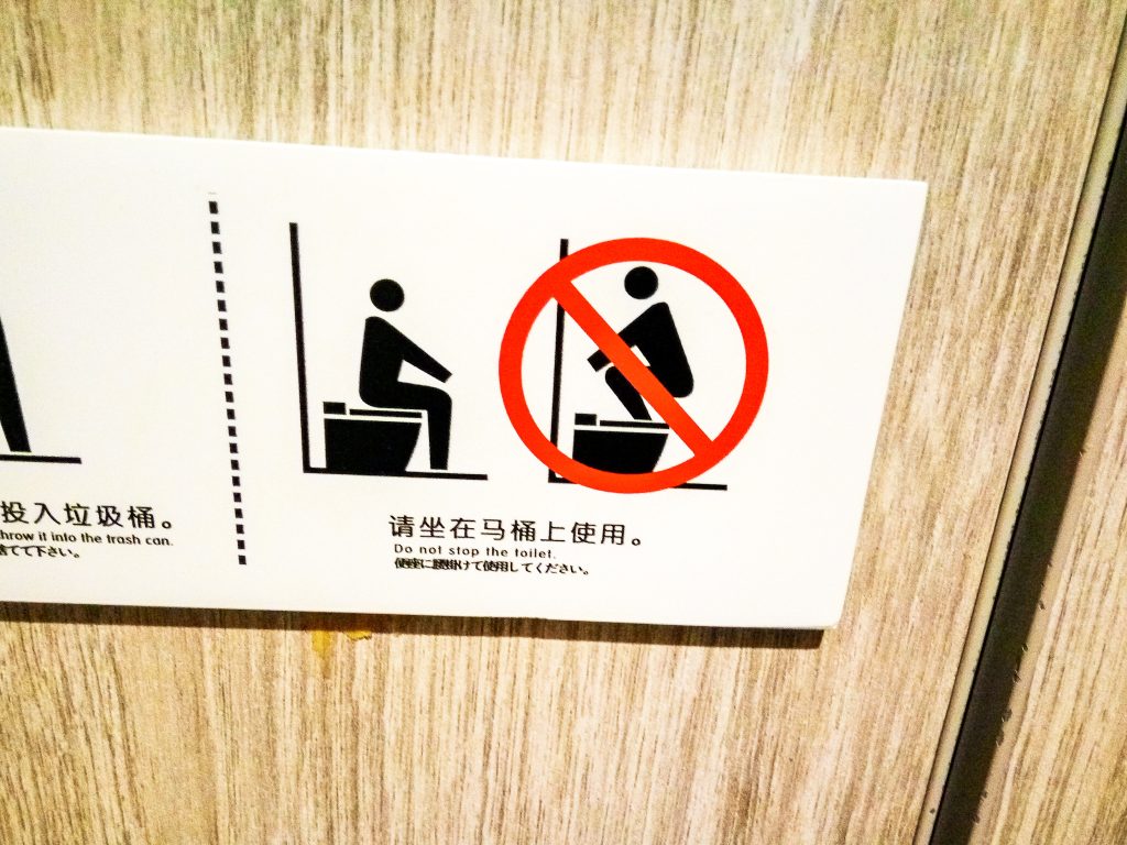 Piktogramy na wc, ktoré hovoria, že si máte sadnút na wc a nie stúpať naňho. Pod tým popis uvedený v čínštine a následne v angličtine "Do not stop the toilet".