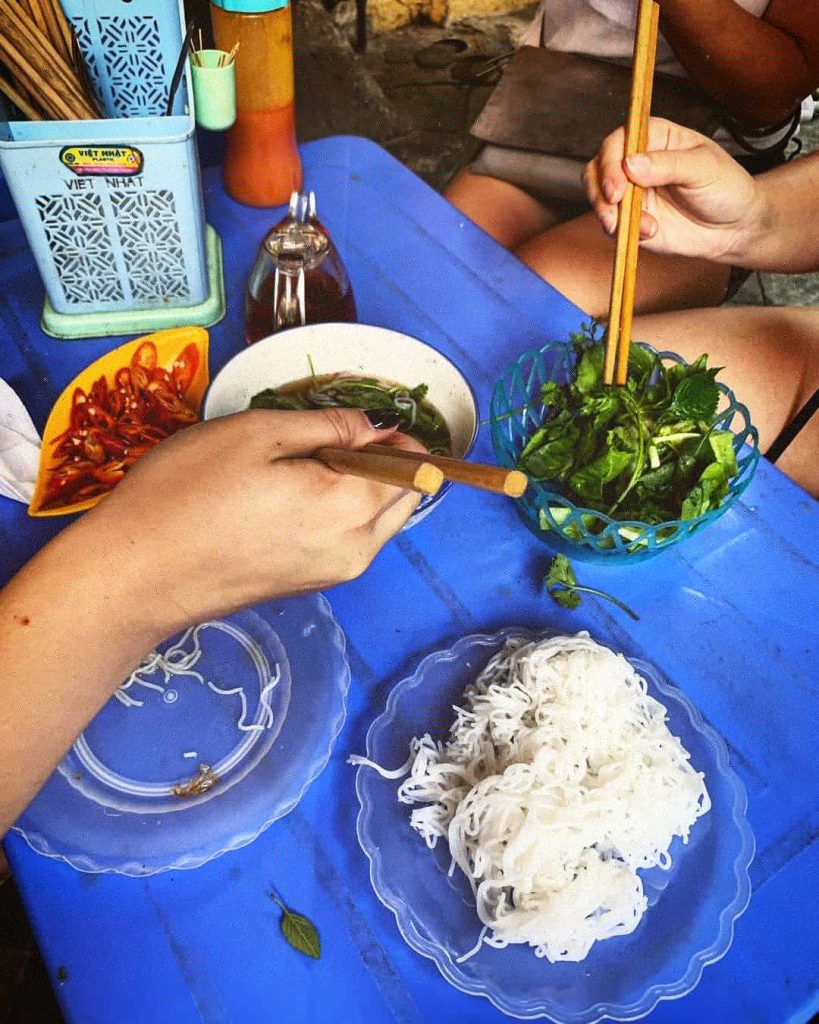 Jedlo na stole a ruky s čínskymi paličkami naťahujúce sa za jedlom