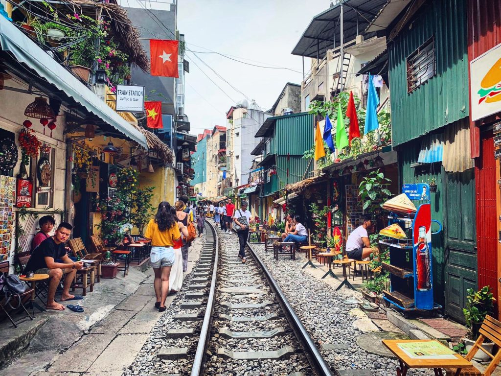 Vlaková ulica vo Vietname, kde po strede ide vlaková trať a po bokoch je množstvo obchodným prevádzok a kaviarní