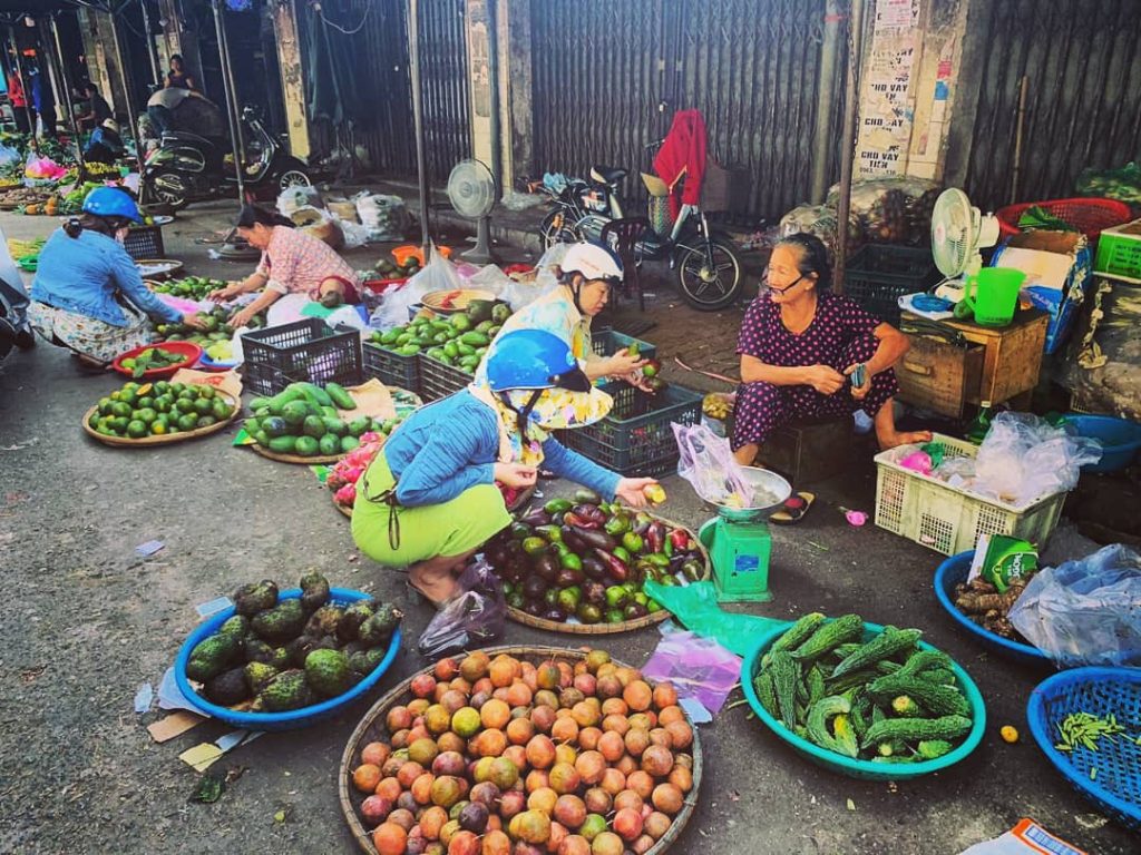 Vietnamky na miestnom trhu predávajú ovocie v obrovských misách ležiacich na zemi