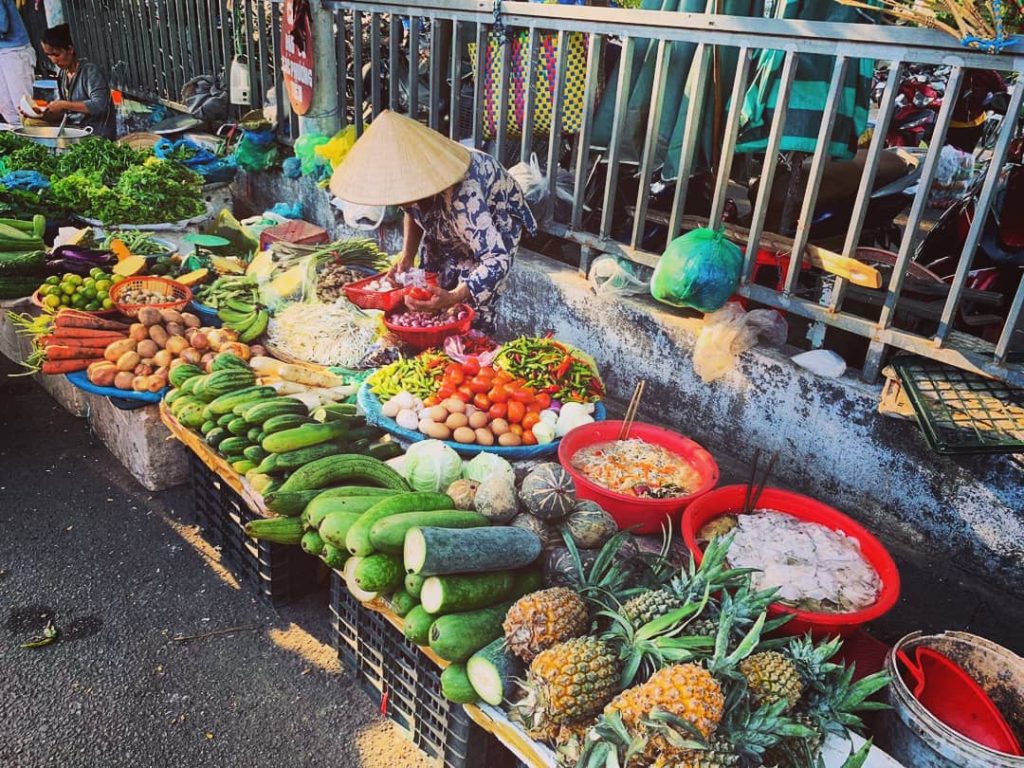 Vietnamka na miestnom trhu predáva rôzne ovocie a zeleninu