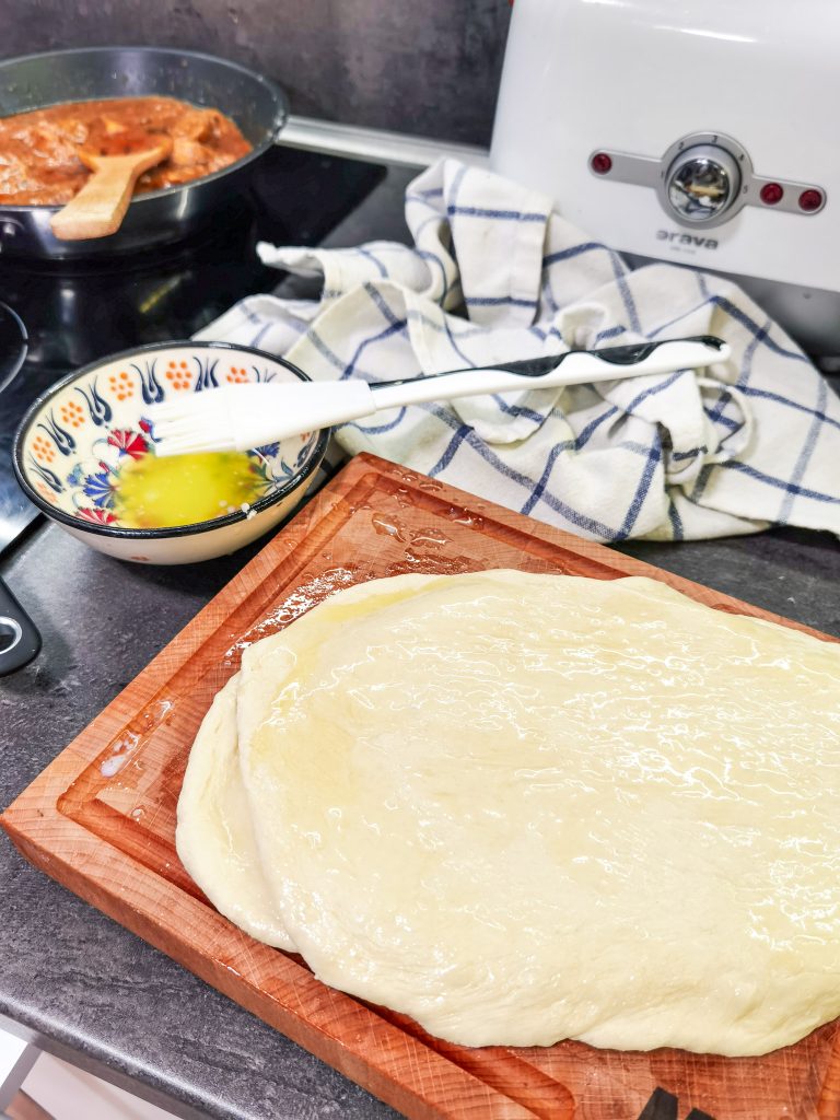 Naany pripravené na pečenie - poukladané na sebe, vyvaľkané a potrené maslom. V pozadí mašľovačka s rozpusteným maslom.