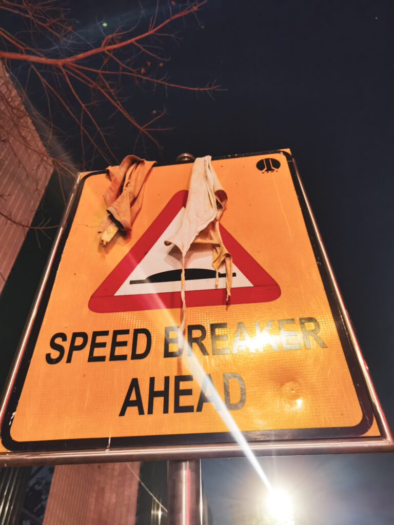 Značka "Speed breaker ahead" a na nej prevesené dva kusy zničeného oblečenia